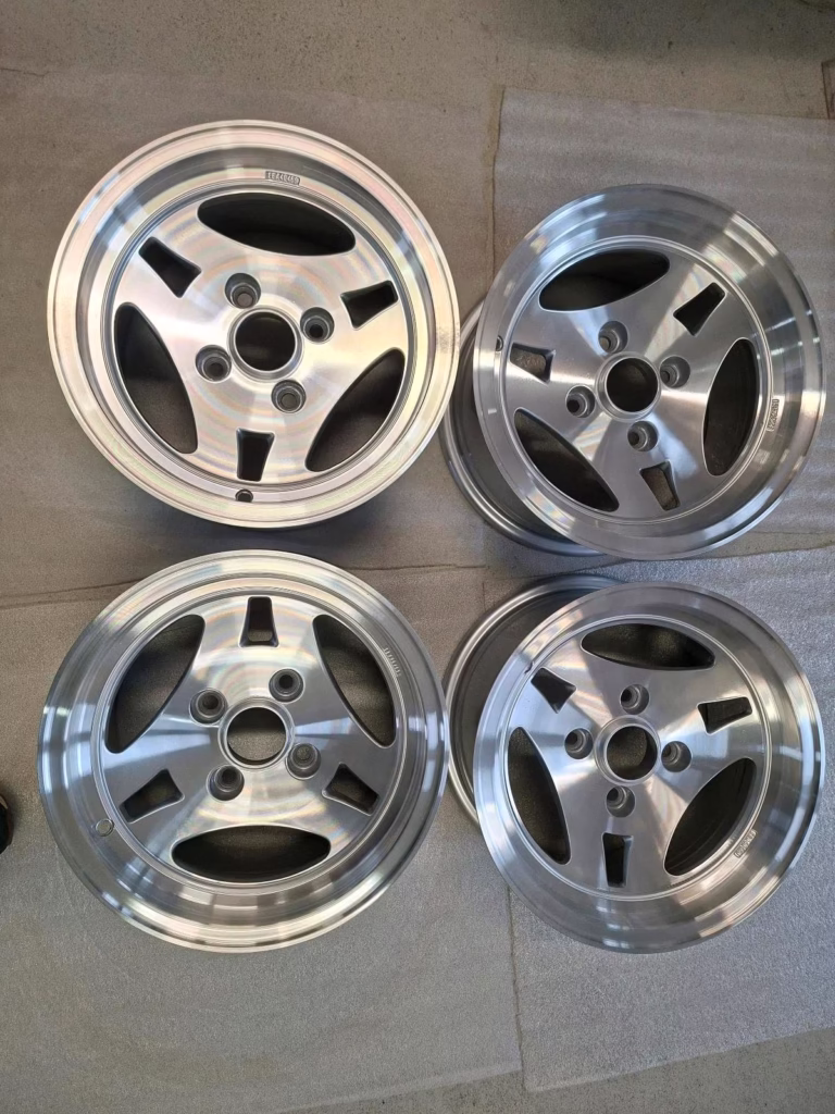 Vier Ats Ford Capri Escort Felgen 7x13 ET .5 KBA40469 Leichtmetallräder, jedes mit fünf Speichen, sind auf Beton dargestellt-zwei ruhen auf weißer Polsterung-perfekt für die Aufrüstung Ihres Ford Capri oder Escort.