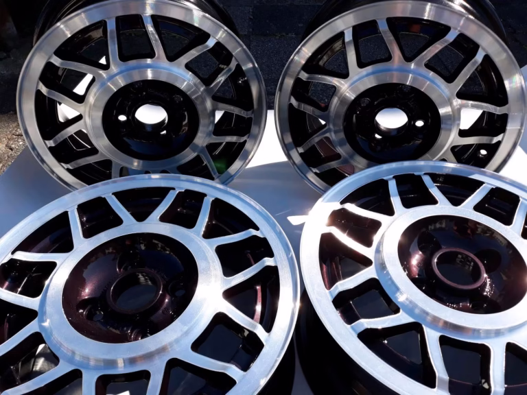 Vier Avus Snowflake Alufelgen Dark Burgundy LC3U für Golf 1 Scirocco im Mehrspeichendesign sind aufrecht und flach auf einer weißen, das Sonnenlicht reflektierenden Fläche angeordnet.