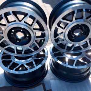 Vier Avus Snowflake Alufelgen Helios Blue La5Y Golf 1 sind paarweise auf einer gepflasterten Fläche gestapelt und glänzen im hellen Sonnenlicht.