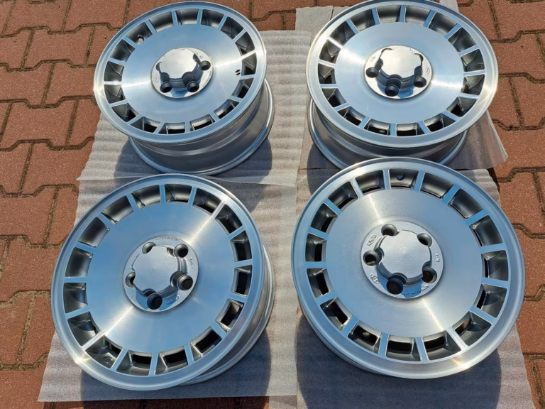 Vier Ford Granada Consul Trx Felgen in Silber werden in einem 2x2-Raster auf Platten über Ziegelsteinpflaster angezeigt, ideal für klassische Fahrzeuge.