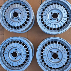 Vier GM Ronal Opel Rekord Felgen Aufbereitet 5.5x14 silberne Leichtmetallräder mit Mehrfachspeichen sind in einem Quadrat auf einer Kartonfläche über Ziegelpflaster angeordnet.