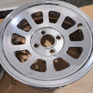 Ein polierter Mini Cooper Alufelgen Hochglanzverdichtet 6x13 verfügt über zehn ovale Speichen und eine zentrale Nabe, die auf einer Kartonoberfläche abgebildet sind - perfekt, um den Stil Ihres Fahrzeugs aufzuwerten.