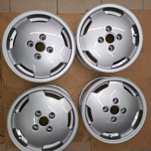 Vier silberne Ronal Audi 80 90 Felgen 393601025A mit je fünf Radmuttern sind in einem rechteckigen Muster auf einem gekachelten Boden mit Kartonunterlage angeordnet - perfekt für Audi-Liebhaber.