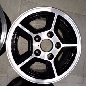 Eine Nahaufnahme einer schwarz-silbernen Ronal Felgen Opel Manta Senator Kapitän Commodore Leichtmetallfelge auf einer gepolsterten Oberfläche.