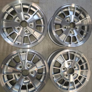 Die vier Ronal Kleeblatt Felgen, Modell 75GB10007AA, sind in einem Quadrat auf einer beigen Oberfläche angeordnet - ideal für Ihren Ford Granada Consul.