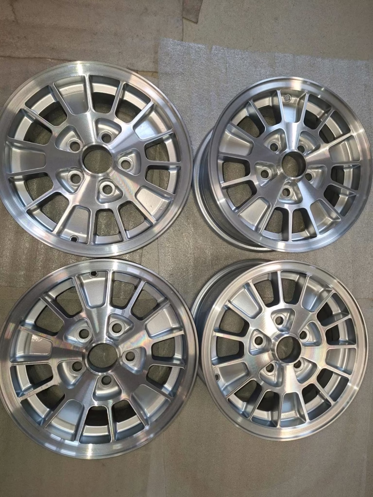 Die vier Ronal Kleeblatt Felgen, Modell 75GB10007AA, sind in einem Quadrat auf einer beigen Oberfläche angeordnet - ideal für Ihren Ford Granada Consul.