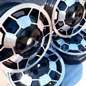 Vier Saab 900 90 Alufelgen Fußbal Felgen 5.5x15, in schwarz und silber, gestapelt auf einer gepflasterten Fläche bei Tageslicht.