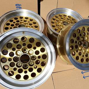 Vier goldene Mehrspeichen-Leichtmetallräder mit polierten silbernen Felgen werden im Freien auf flachgedrückte Kartons gestellt.